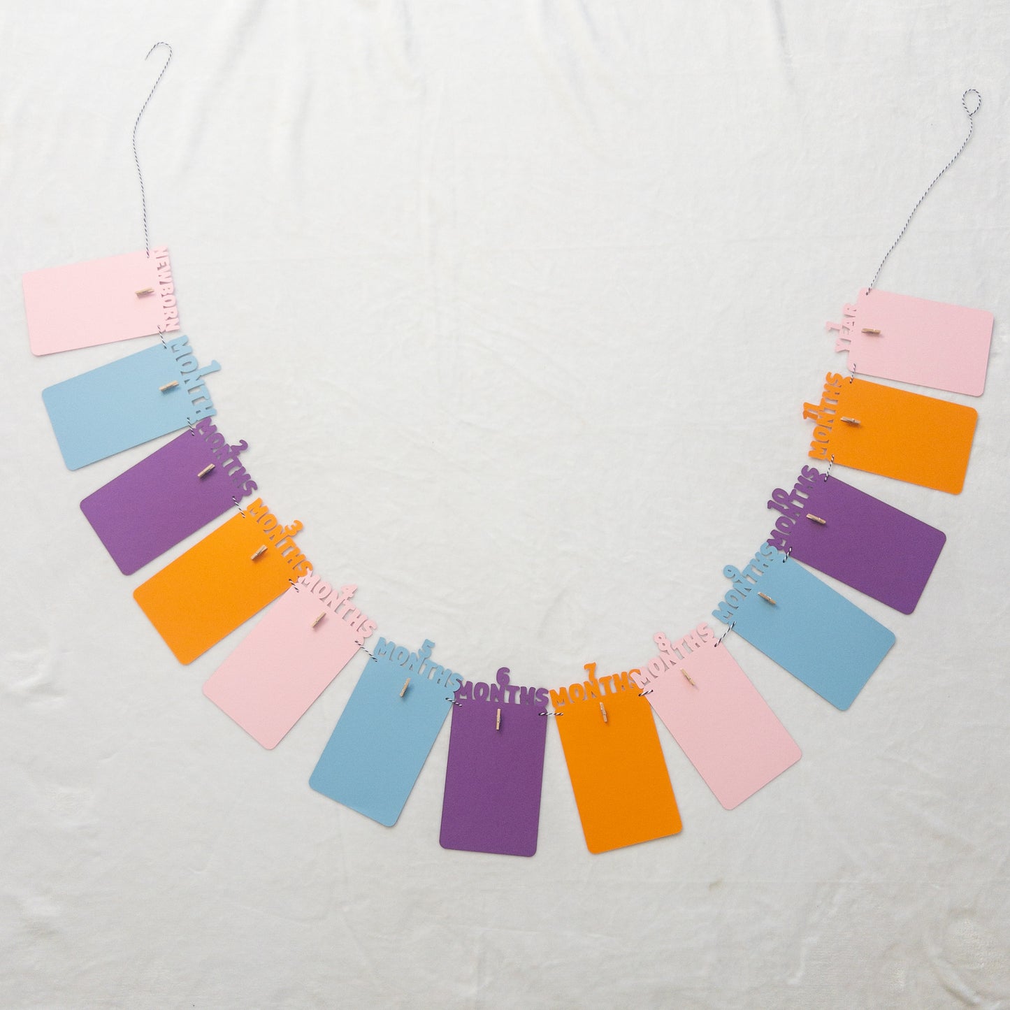 A colorful banner made of paper in purple, orange, pink, and blue, each with a photo clip attached to it, strung together with a string.
