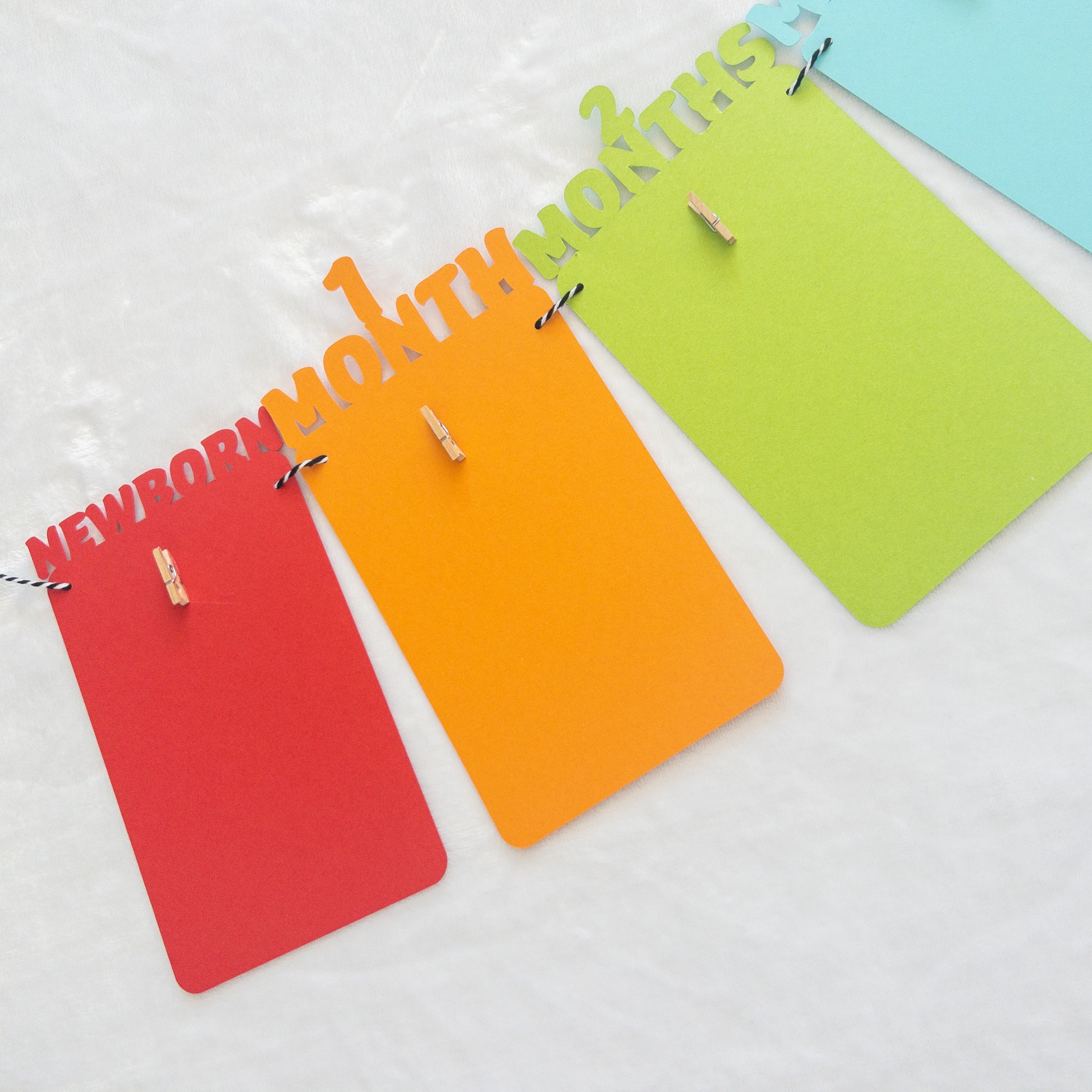 A colorful banner made of paper in red, orange, green, and blue, each with a photo clip attached to it, strung together with a string.
