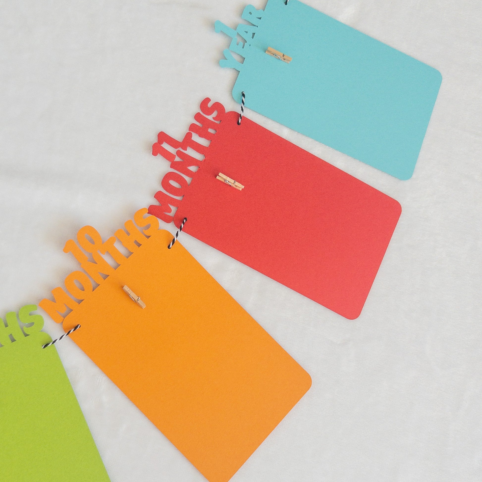 A colorful banner made of paper in red, orange, green, and blue, each with a photo clip attached to it, strung together with a string.