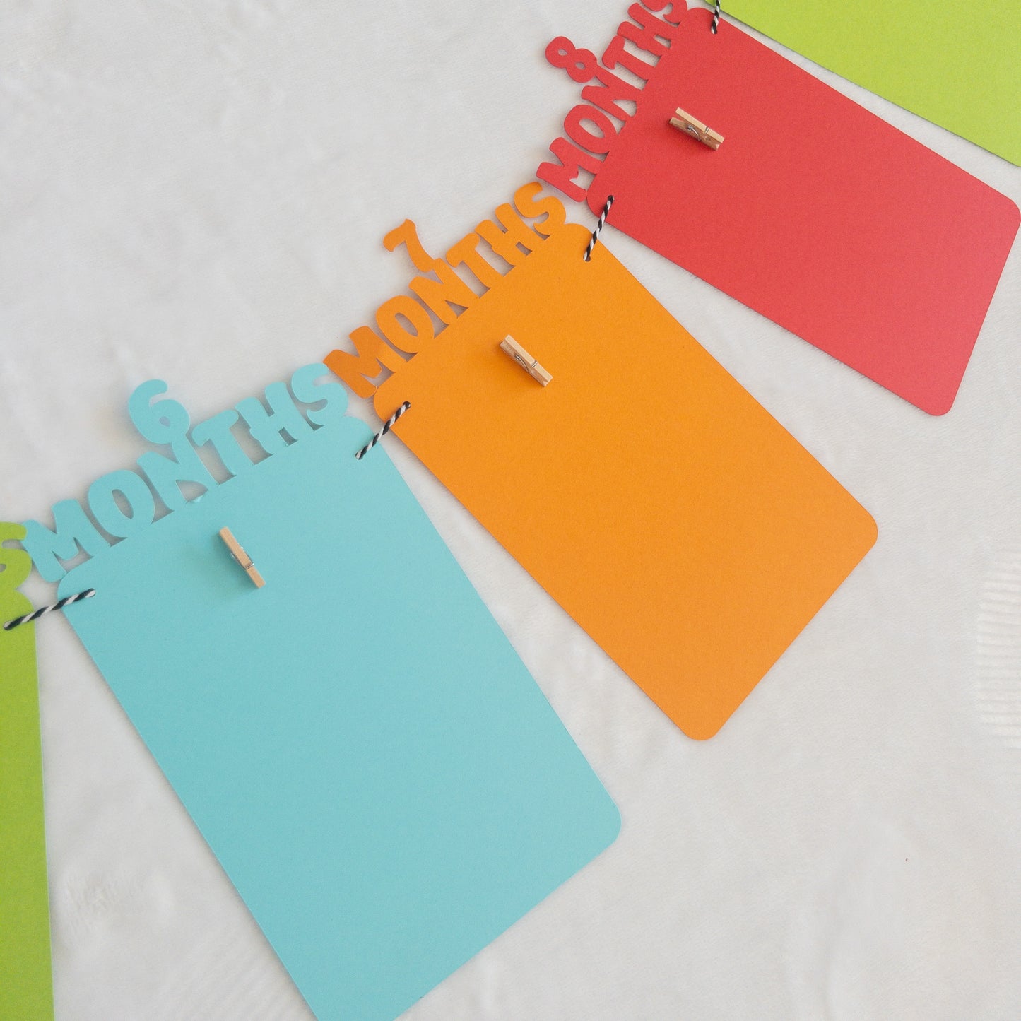 A colorful banner made of paper in red, orange, green, and blue, each with a photo clip attached to it, strung together with a string.
