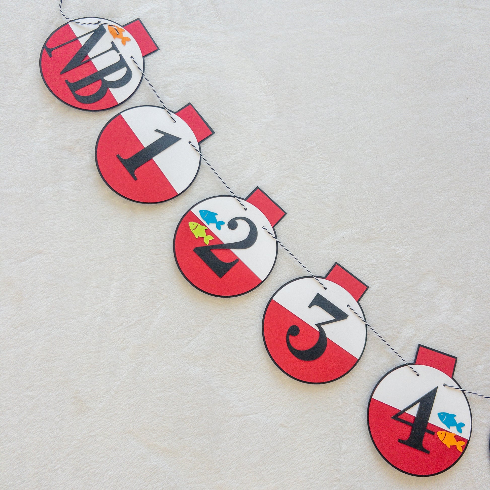 A custom banner featuring a series of round, red and white paper fishing bobbers with numbers representing months, strung on a string.