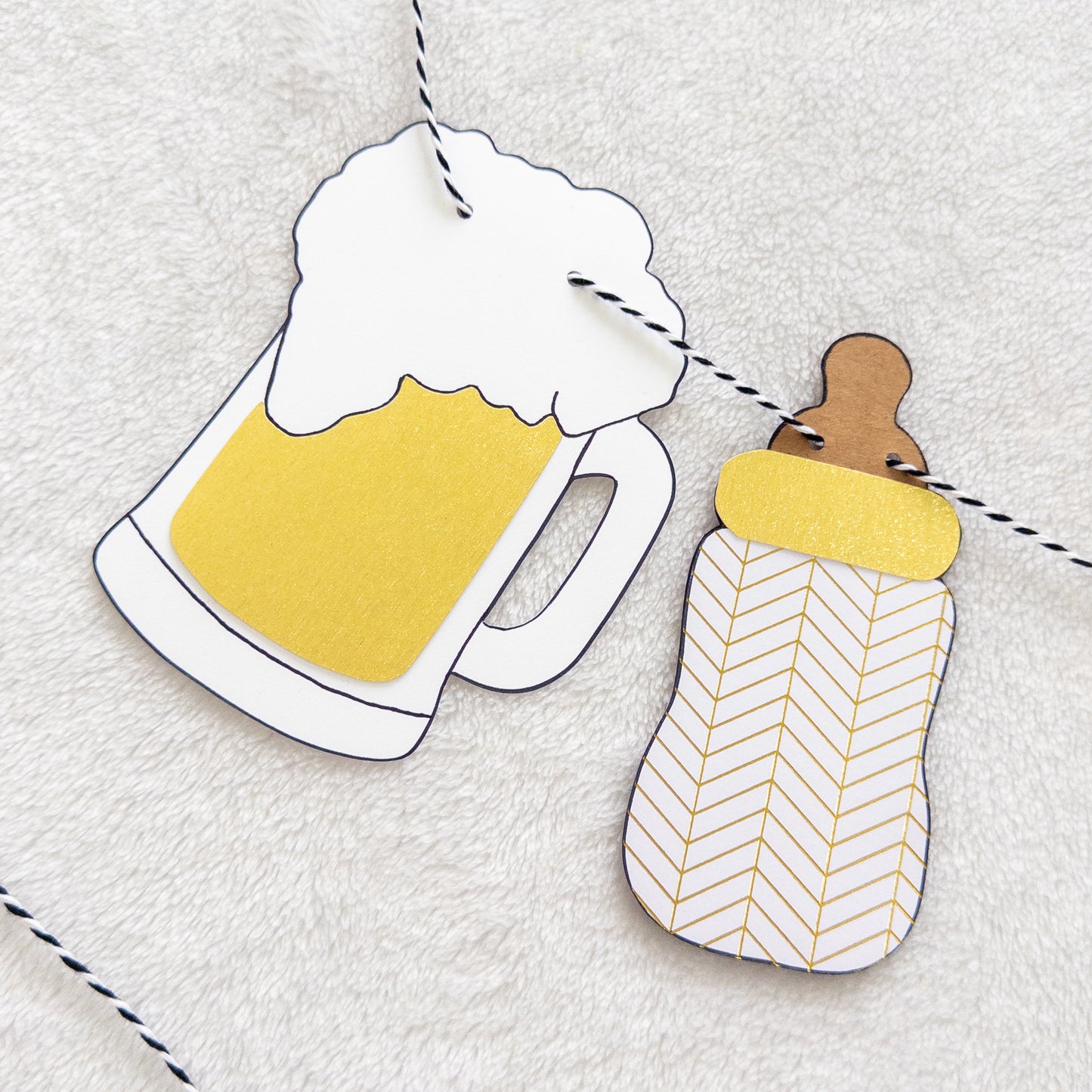 Decorative paper cutout of a beer mug and baby bottle on a textured surface