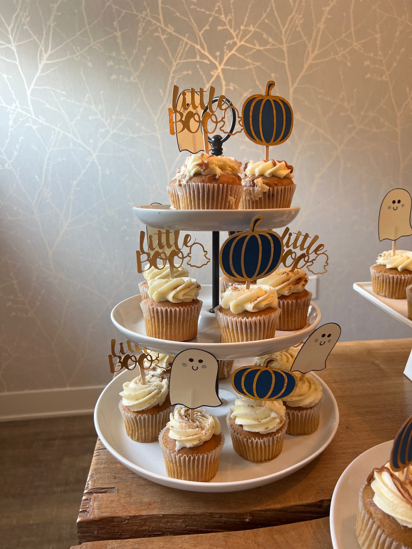 Cupcake toppers with wooden sticks, one designed as a ghost, 'Little Boo' text, and the other shaped like a pumpkin