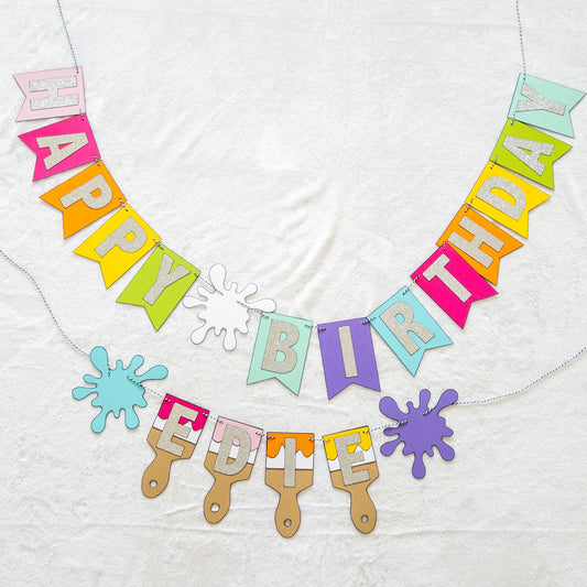 Features the words ‘happy birthday’ in bright and colorful paper. Includes the birthday girl’s name on paint brushes. The letters are made of kit sparkly silver. There are paint splatters on each side of the name.