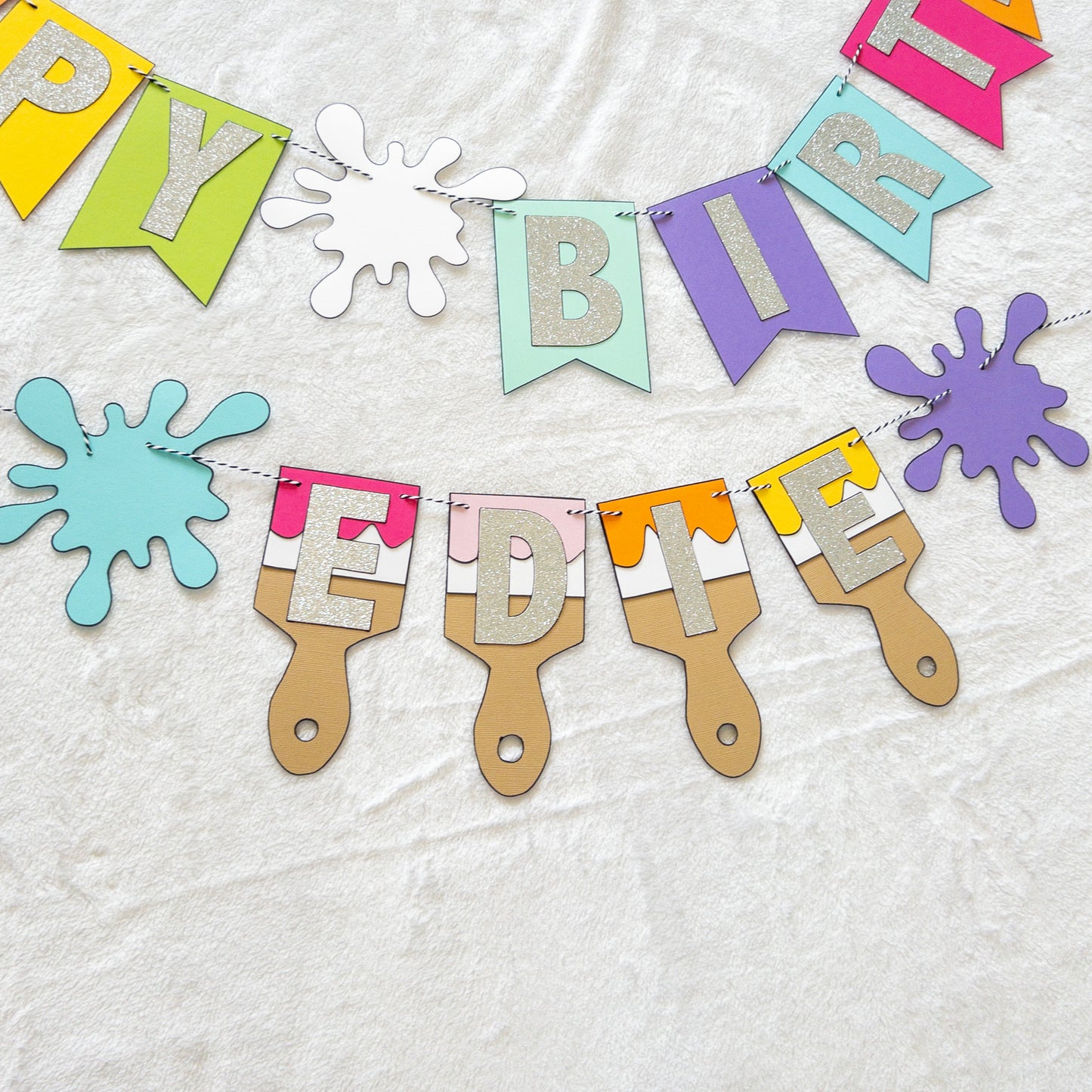 Features the words ‘happy birthday’ in bright and colorful paper. Includes the birthday girl’s name on paint brushes. The letters are made of kit sparkly silver. There are paint splatters on each side of the name.