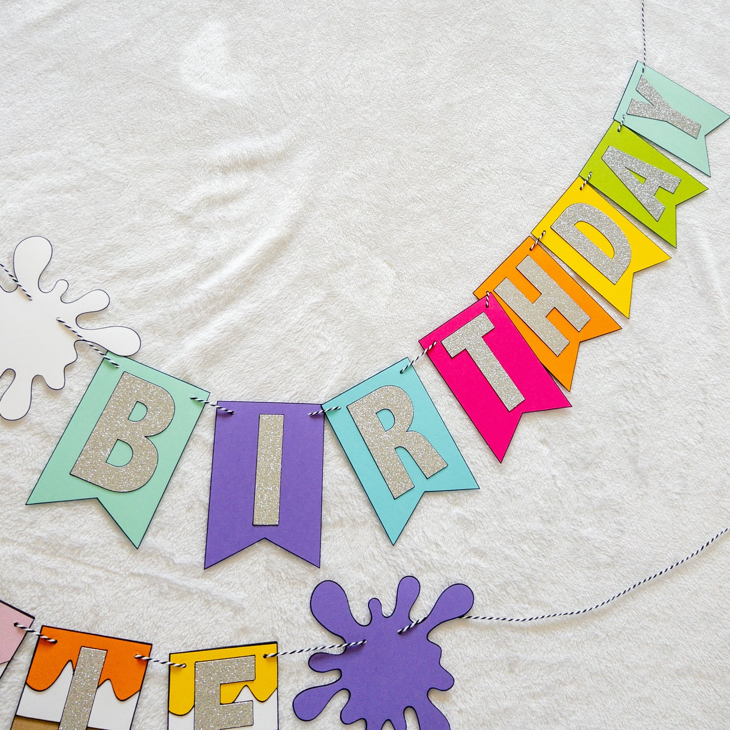 Features the words ‘happy birthday’ in bright and colorful paper. Includes the birthday girl’s name on paint brushes. The letters are made of kit sparkly silver. There are paint splatters on each side of the name.