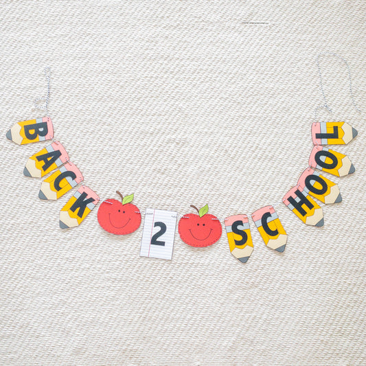 A 'Back to School' themed banner made of paper letters spelling out the phrase, with decorative elements such as apples and pencils, and a piece of lined paper.