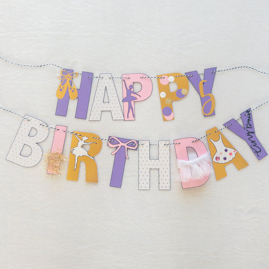 A Happy Birthday banner with the words 'HAPPY BIRTHDAY' in bold letters, decorated with small purple, pink, and yellow details, such as ballet shoes and a tutu, strung on a string.
