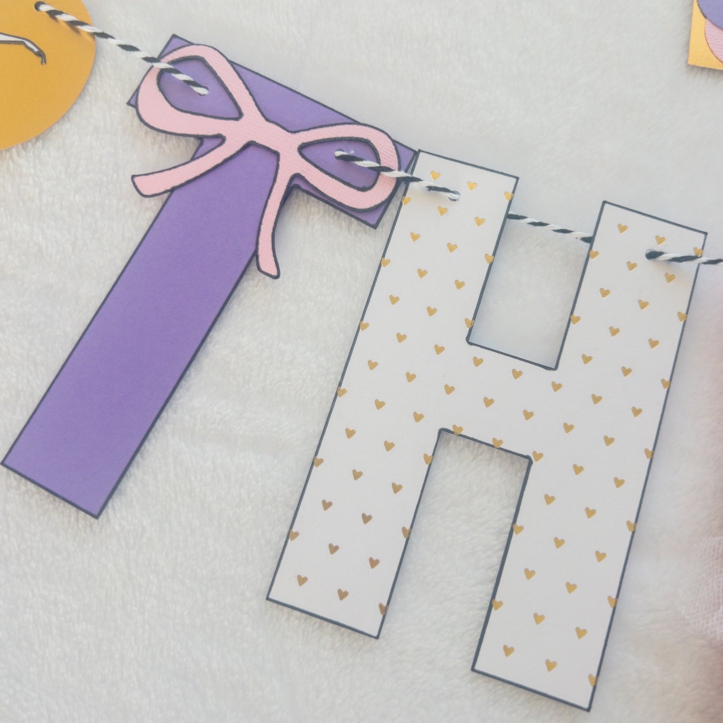 A Happy Birthday banner with the words 'HAPPY BIRTHDAY' in bold letters, decorated with small purple, pink, and yellow details, such as ballet shoes and a tutu, strung on a string.