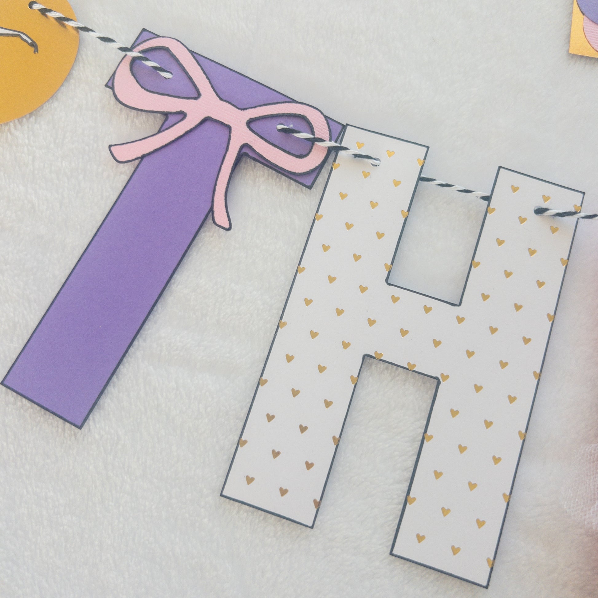 A Happy Birthday banner with the words 'HAPPY BIRTHDAY' in bold letters, decorated with small purple, pink, and yellow details, such as ballet shoes and a tutu, strung on a string.