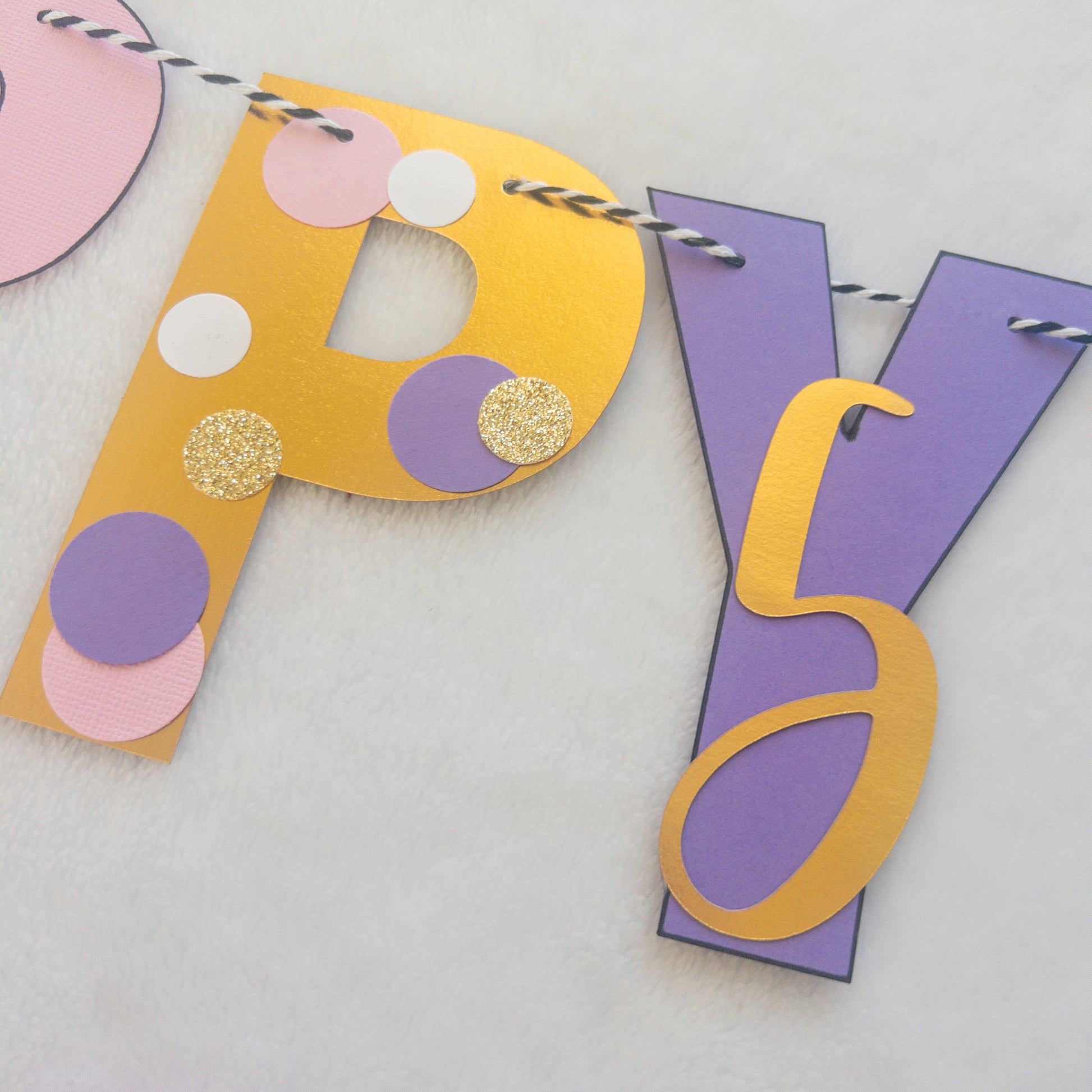 A Happy Birthday banner with the words 'HAPPY BIRTHDAY' in bold letters, decorated with small purple, pink, and yellow details, such as ballet shoes and a tutu, strung on a string.