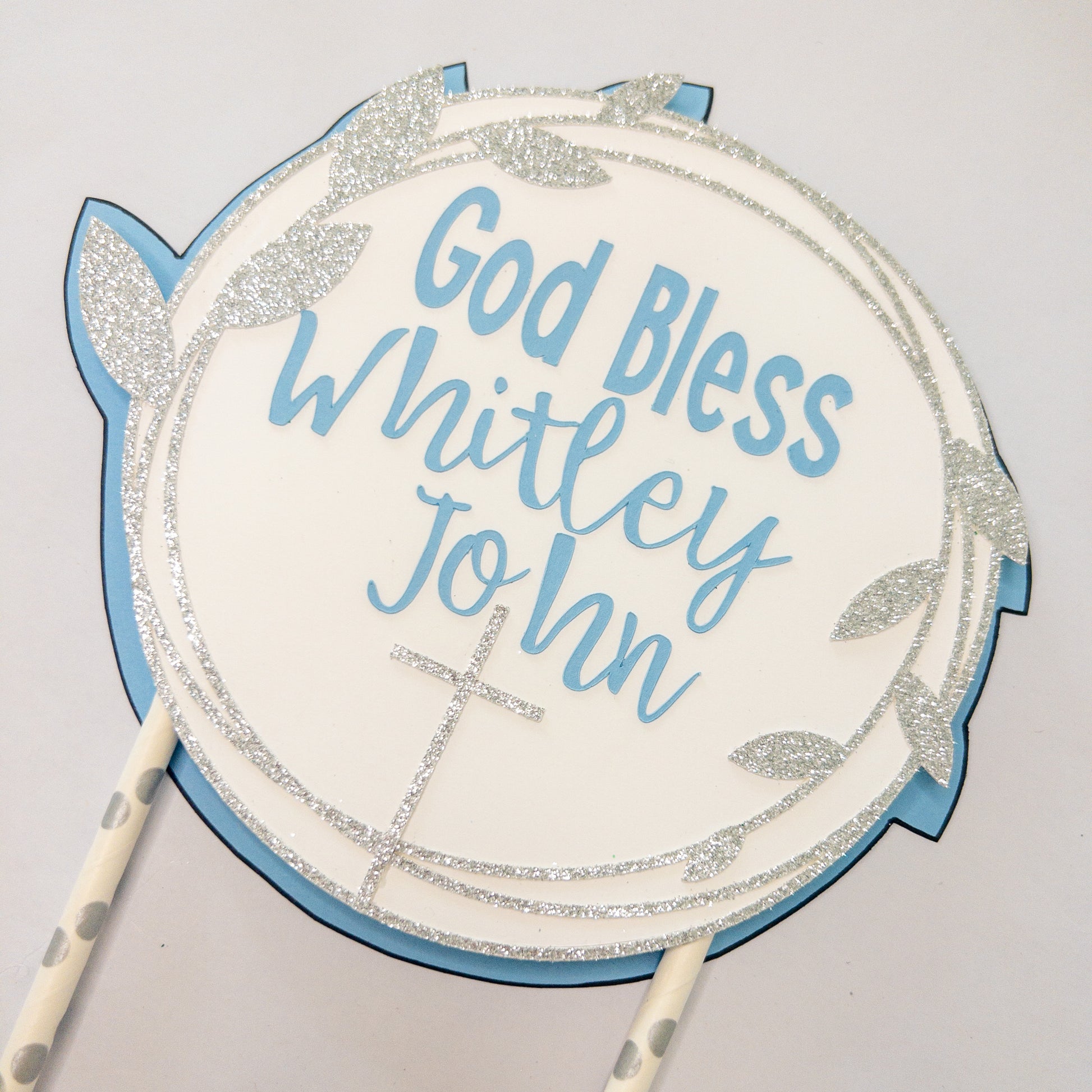 A cake topper with a white background, blue text, and decorative flowers, designed for a baptism or christening celebration.