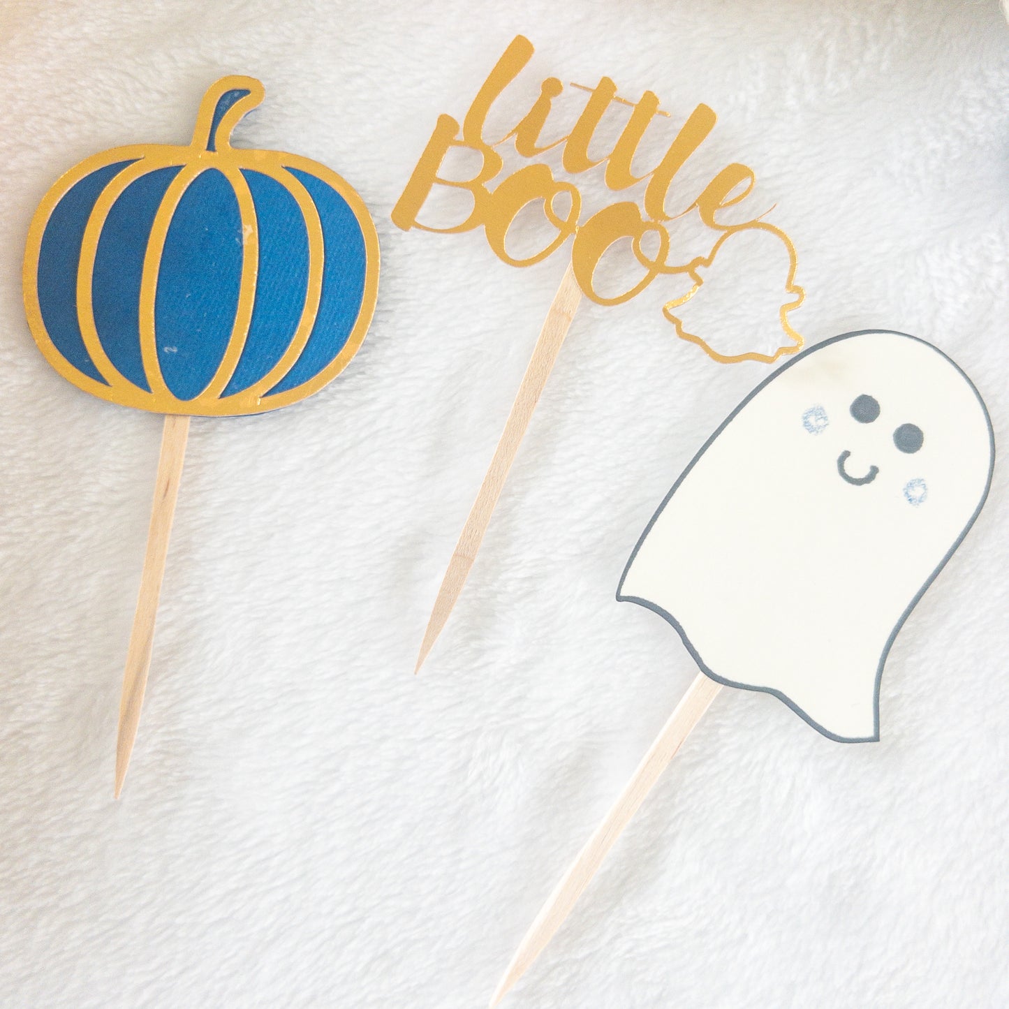 Cupcake toppers with wooden sticks, one designed as a ghost, 'Little Boo' text, and the other shaped like a pumpkin