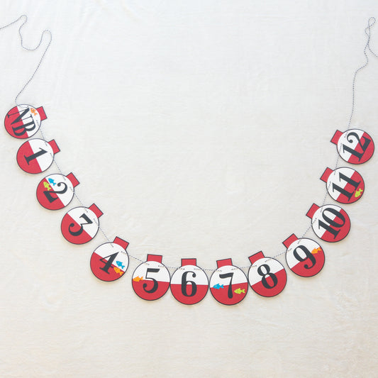 A custom banner featuring a series of round, red and white paper fishing bobbers with numbers representing months, strung on a string.