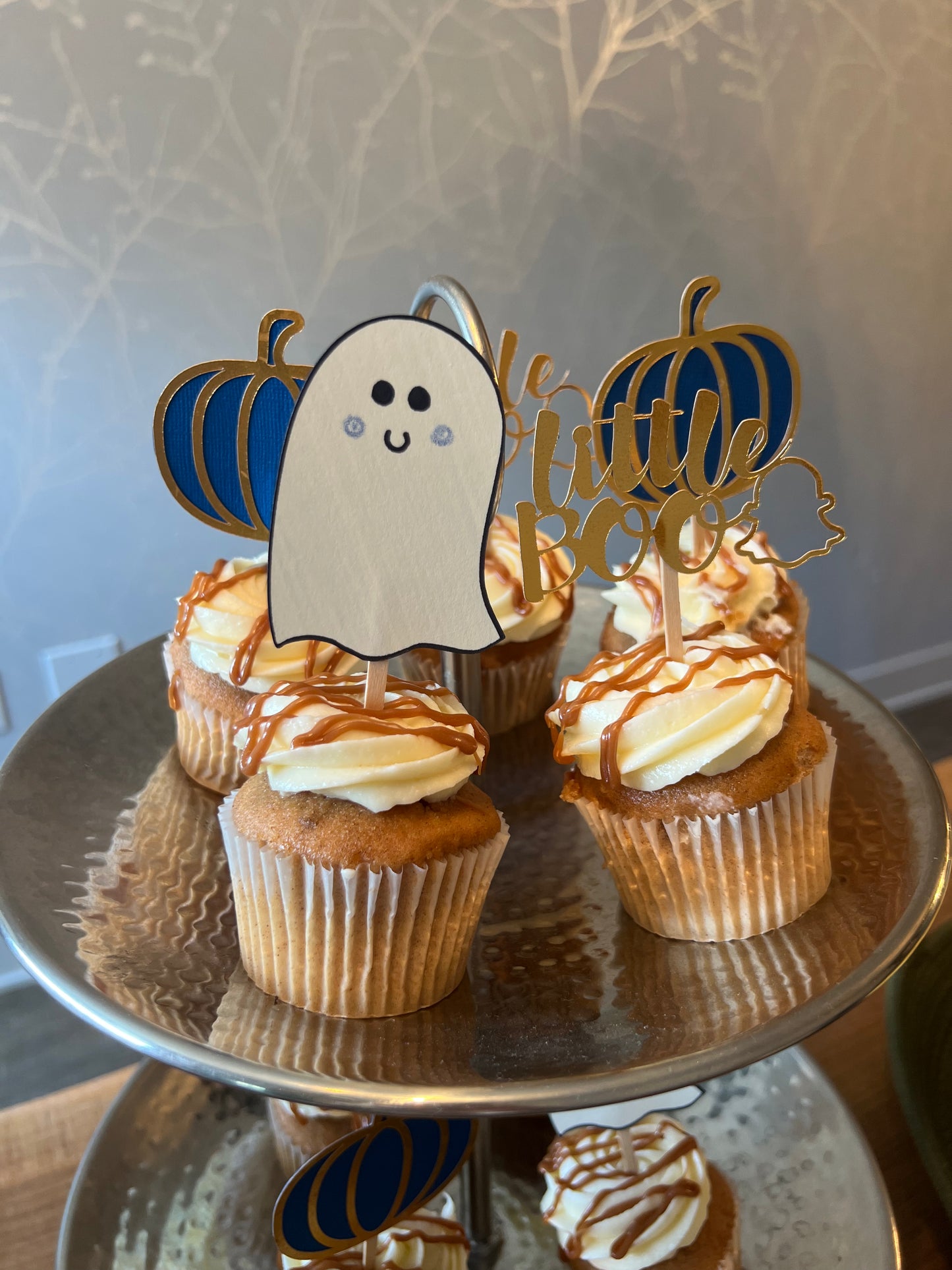 Cupcake toppers with wooden sticks, one designed as a ghost, 'Little Boo' text, and the other shaped like a pumpkin