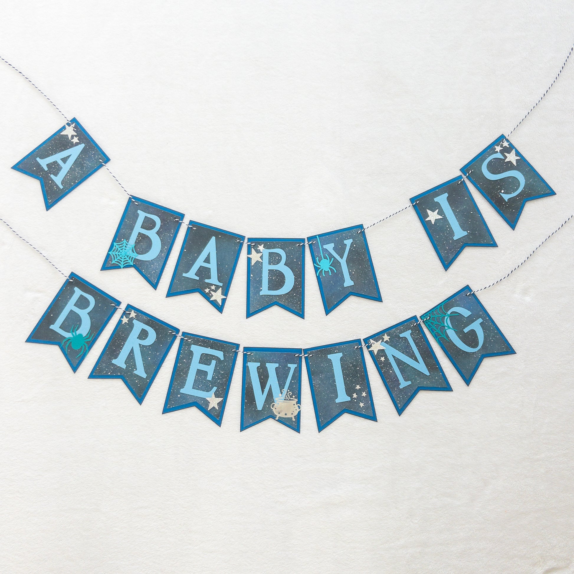 A banner with blue paper letters spelling 'A BABY IS BREWING' with stars and a blue border