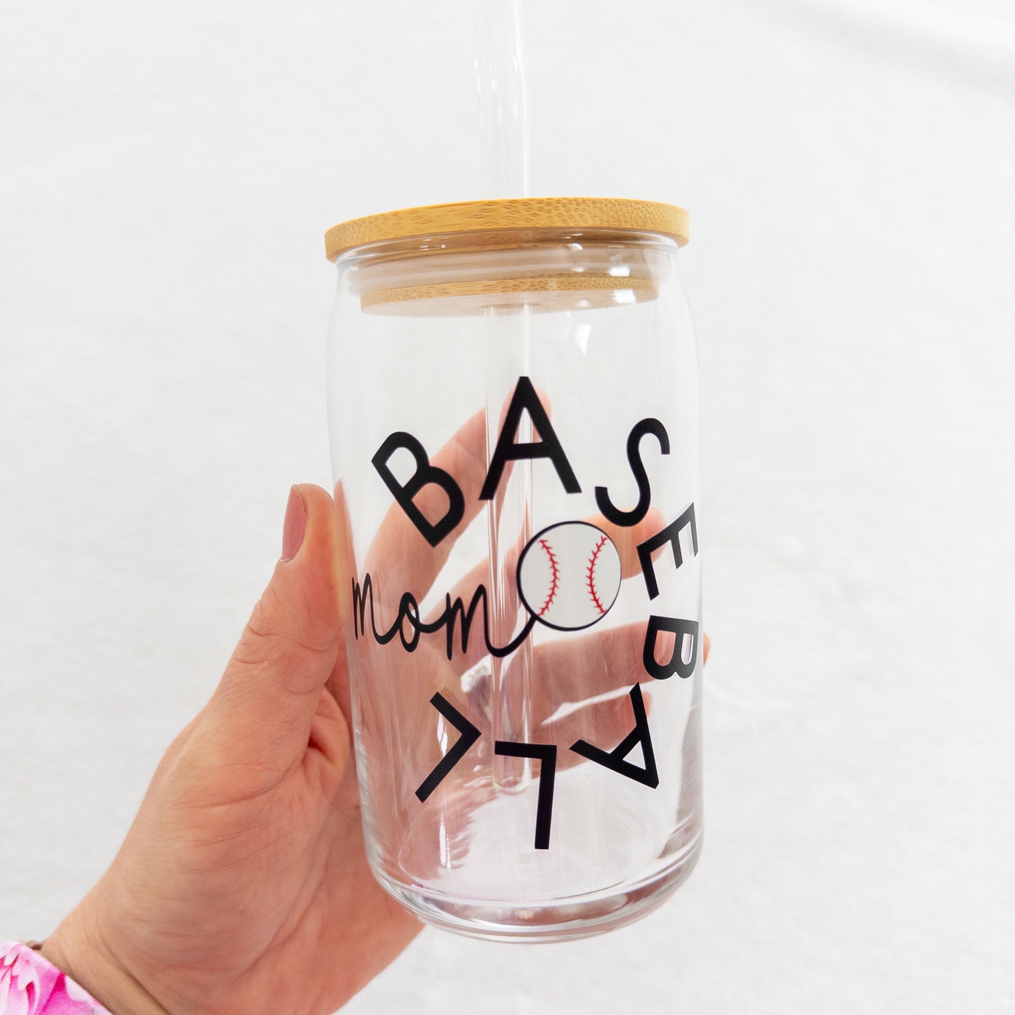 A clear glass cup with a 'Baseball Mom' text and a baseball symbol printed on it, including a straw and a lid.