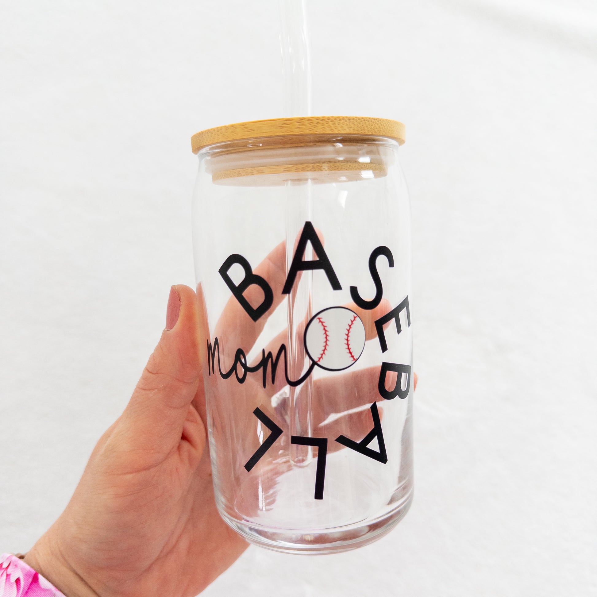 A clear glass cup with a 'Baseball Mom' text and a baseball symbol printed on it, including a straw and a lid.