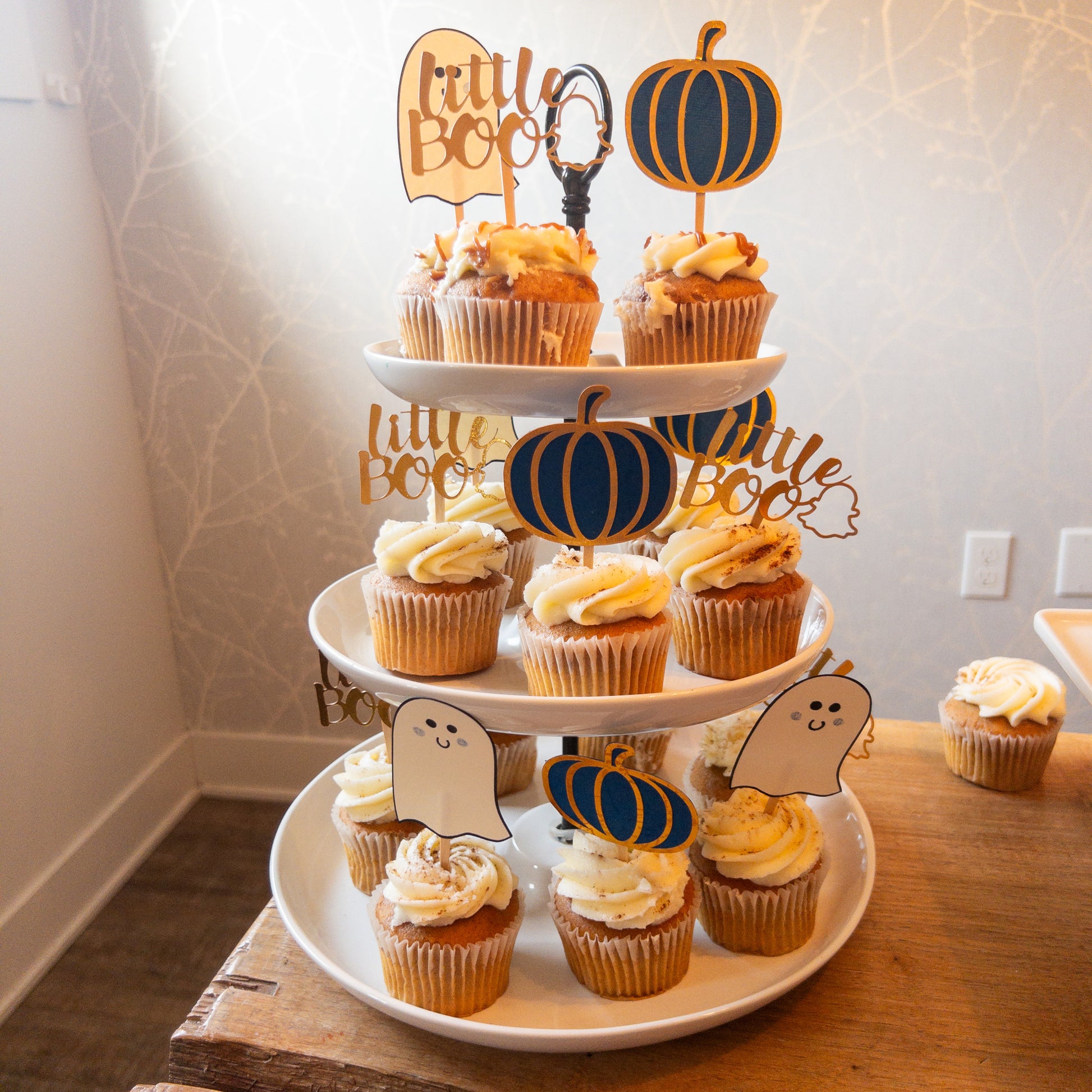 Cupcake toppers with wooden sticks, one designed as a ghost, 'Little Boo' text, and the other shaped like a pumpkin