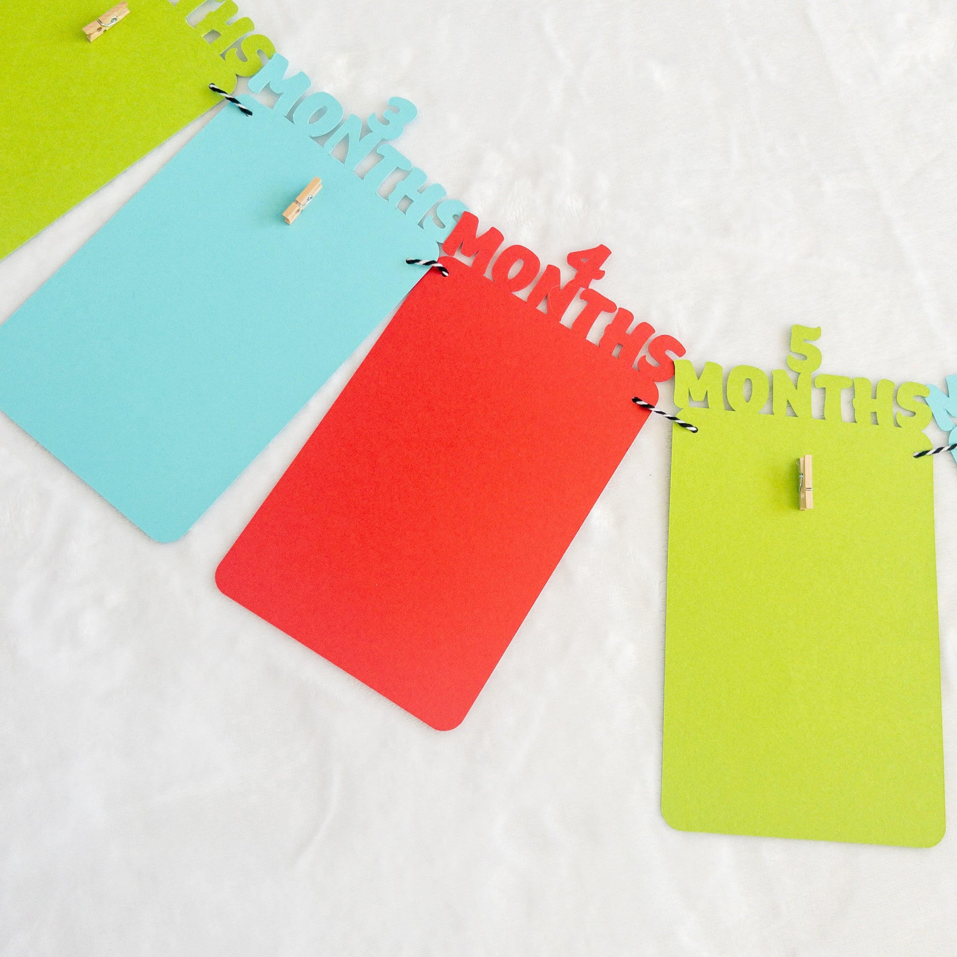 A colorful banner made of paper in red, orange, green, and blue, each with a photo clip attached to it, strung together with a string.