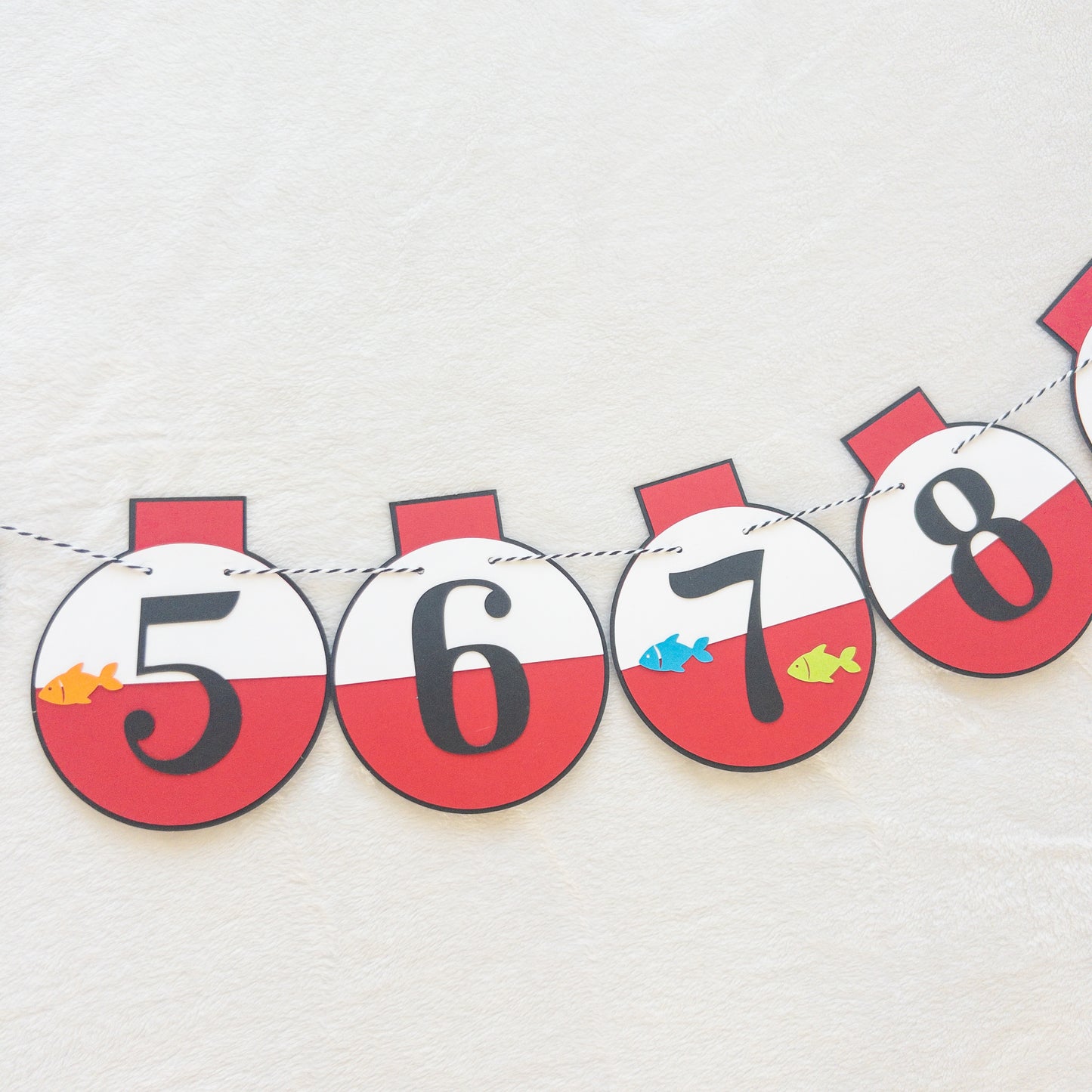 A custom banner featuring a series of round, red and white paper fishing bobbers with numbers representing months, strung on a string.