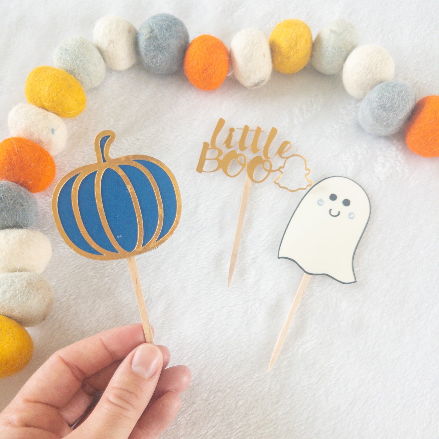 Cupcake toppers with wooden sticks, one designed as a ghost, 'Little Boo' text, and the other shaped like a pumpkin