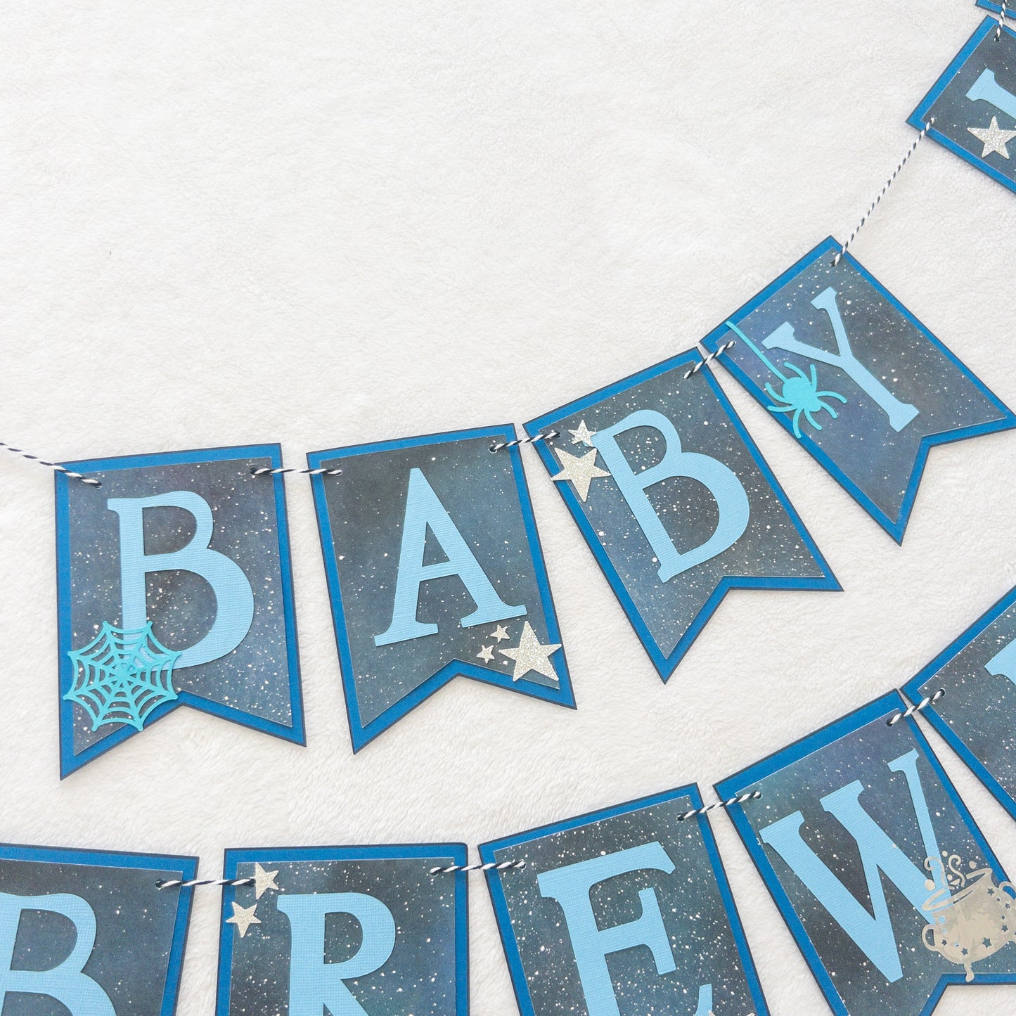 A banner with blue paper letters spelling 'A BABY IS BREWING' with stars and a blue border