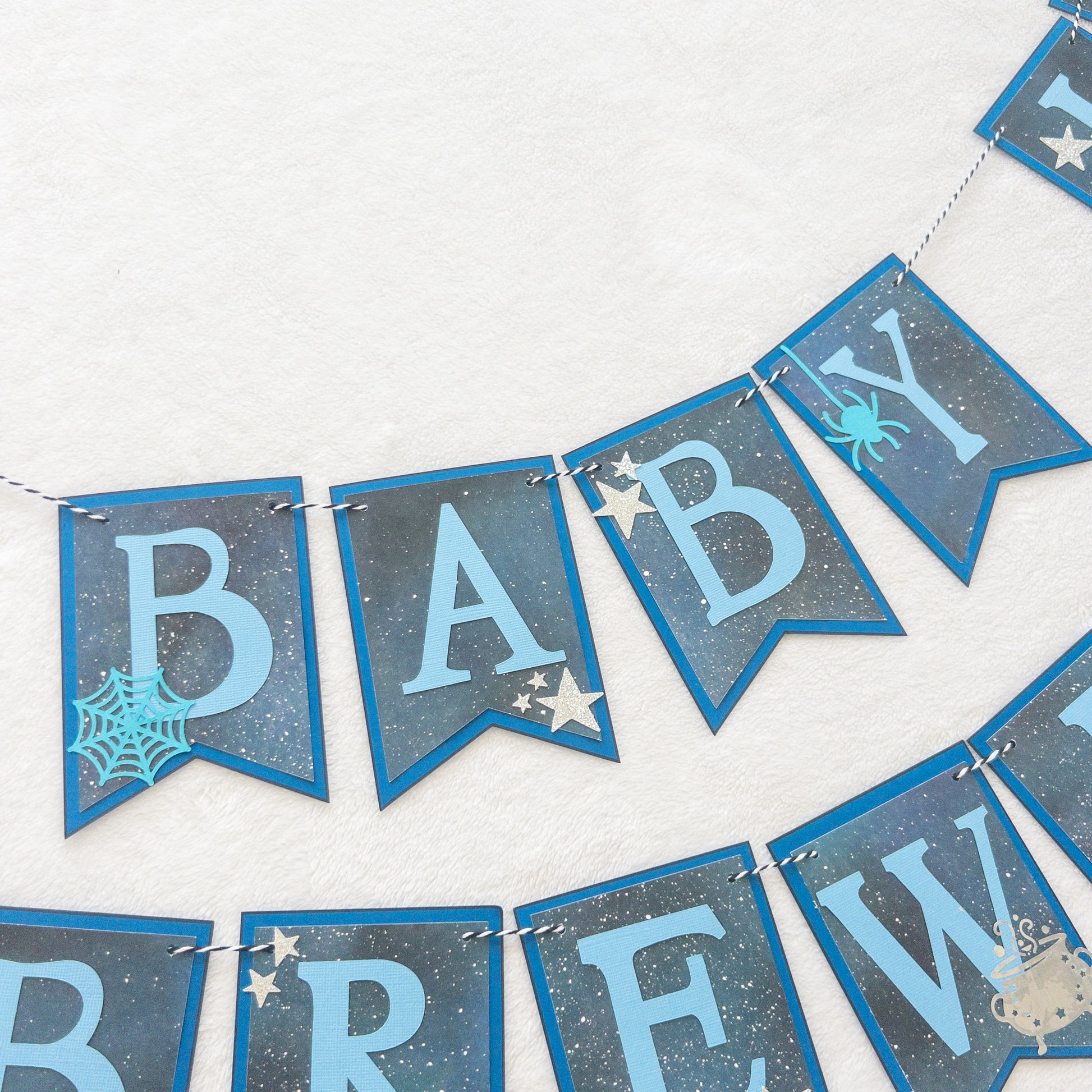 A banner with blue paper letters spelling 'A BABY IS BREWING' with stars and a blue border