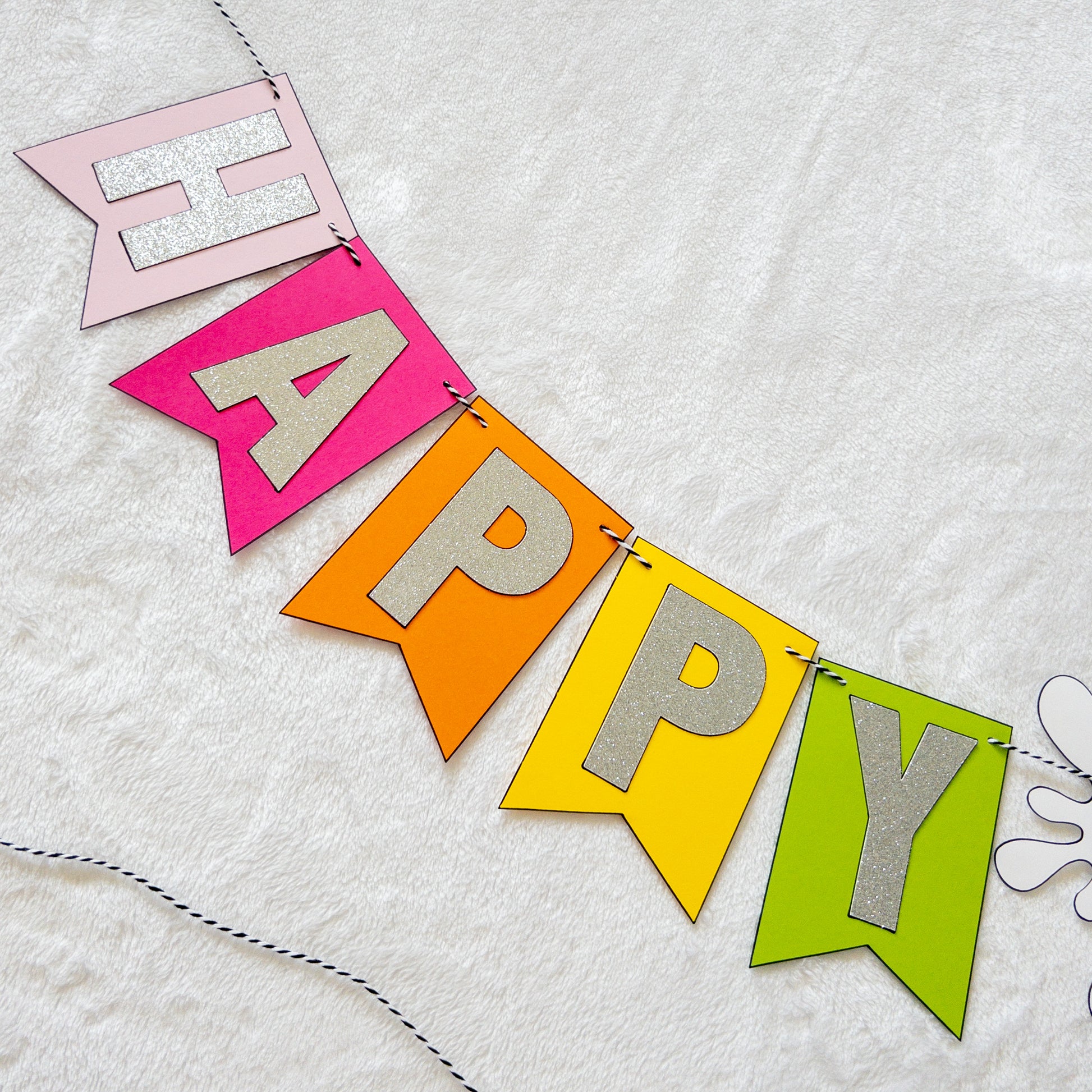 Features the words ‘happy birthday’ in bright and colorful paper. Includes the birthday girl’s name on paint brushes. The letters are made of kit sparkly silver. There are paint splatters on each side of the name.