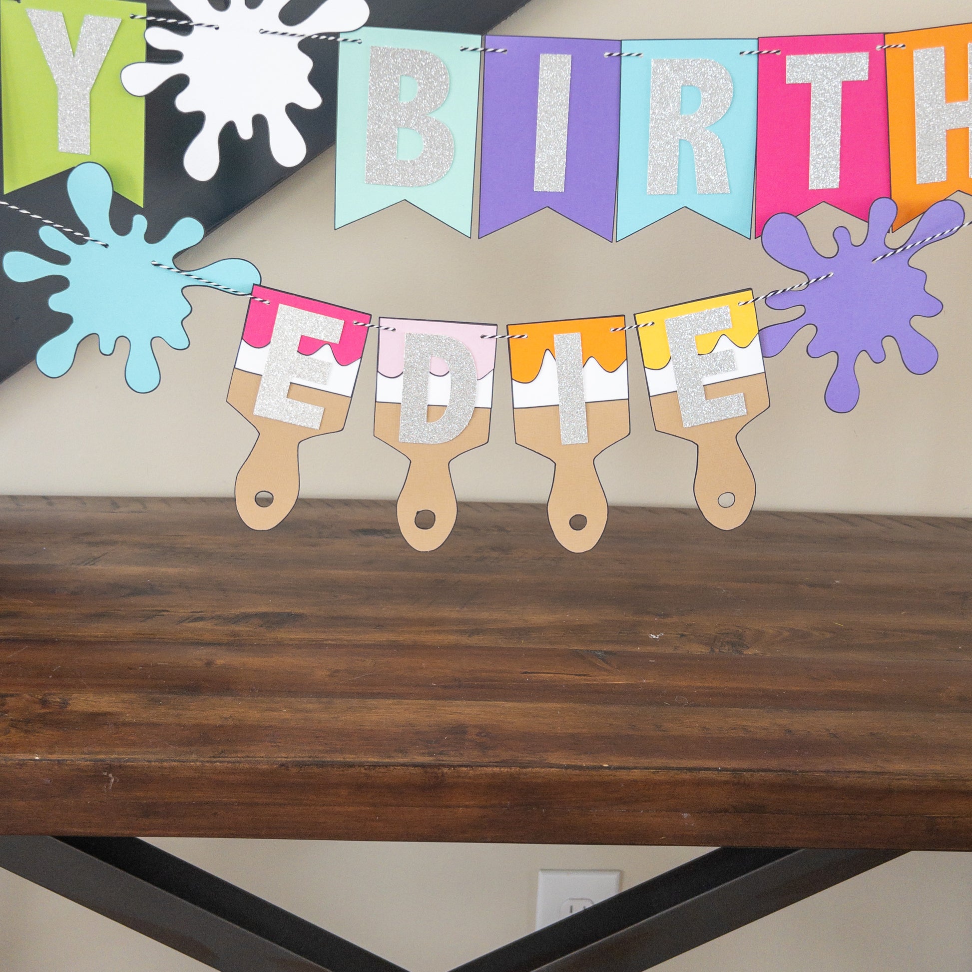 Features the words ‘happy birthday’ in bright and colorful paper. Includes the birthday girl’s name on paint brushes. The letters are made of kit sparkly silver. There are paint splatters on each side of the name.
