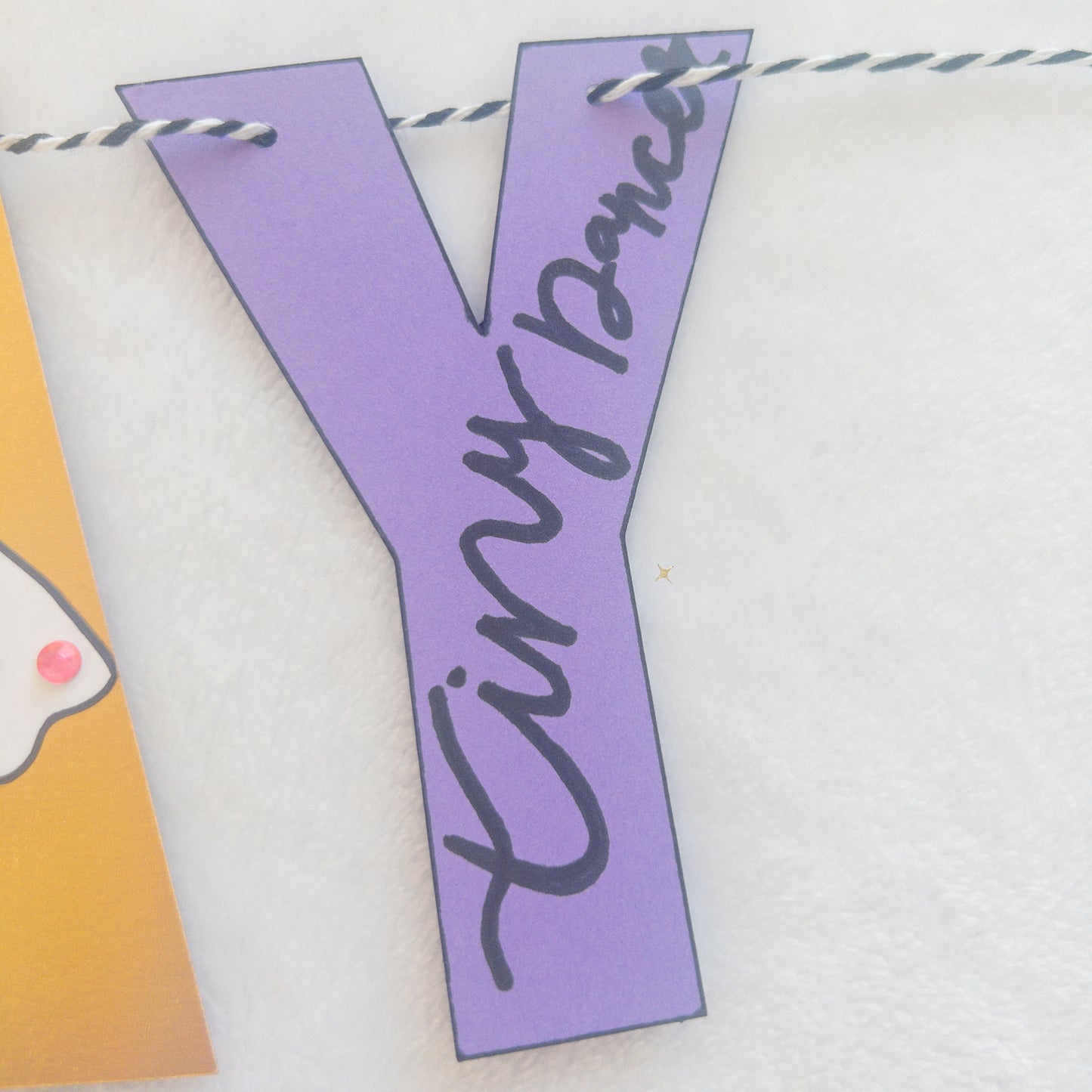 A Happy Birthday banner with the words 'HAPPY BIRTHDAY' in bold letters, decorated with small purple, pink, and yellow details, such as ballet shoes and a tutu, strung on a string.