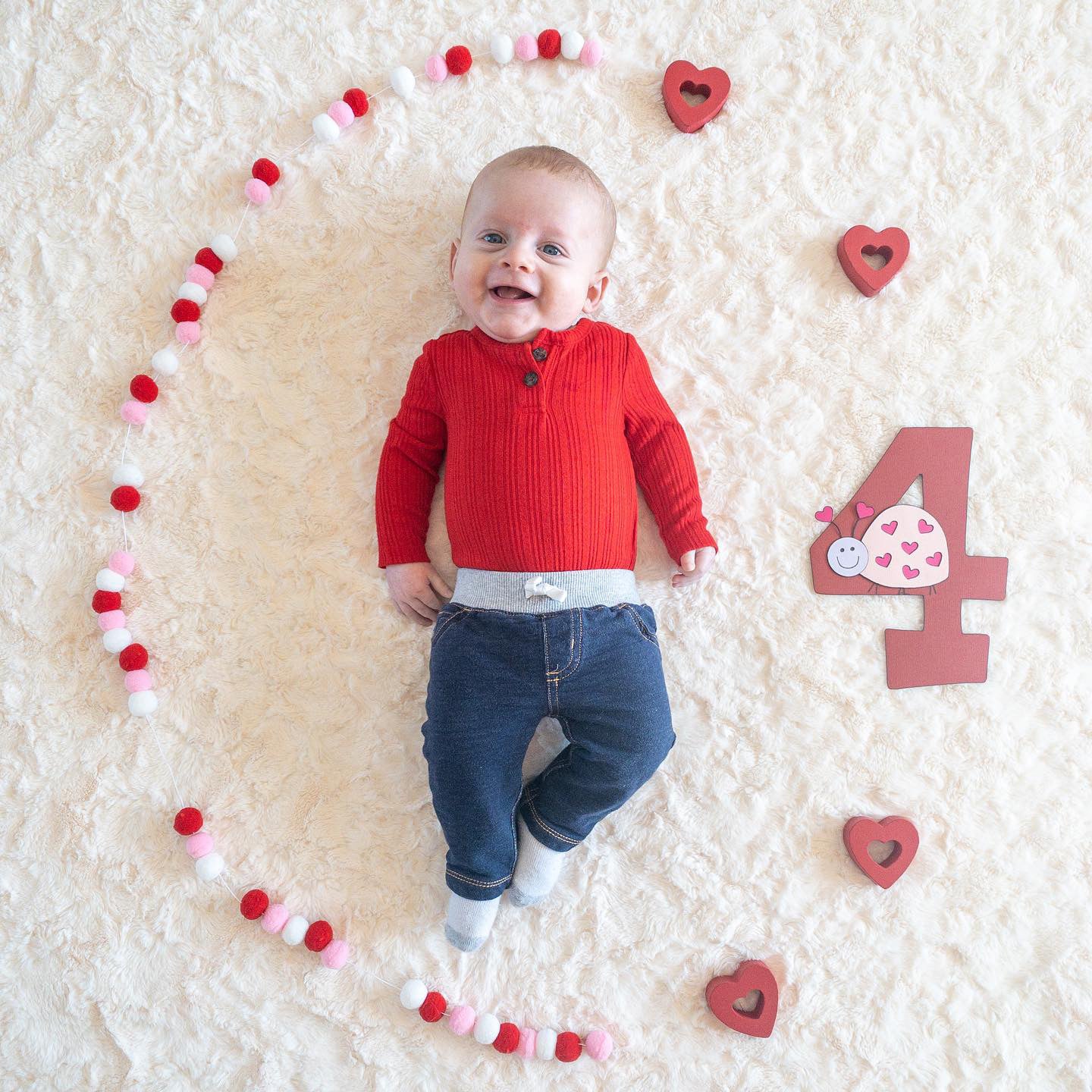 A baby laying on a furry white blanket next to a love bug themed number 