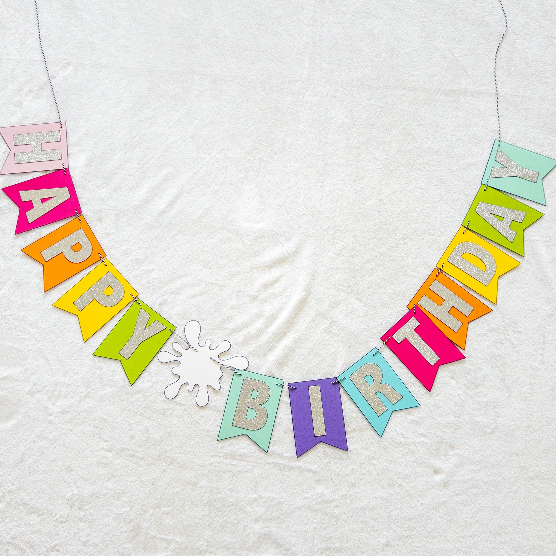 Features the words ‘happy birthday’ in bright and colorful paper. Includes the birthday girl’s name on paint brushes. The letters are made of kit sparkly silver. There are paint splatters on each side of the name.